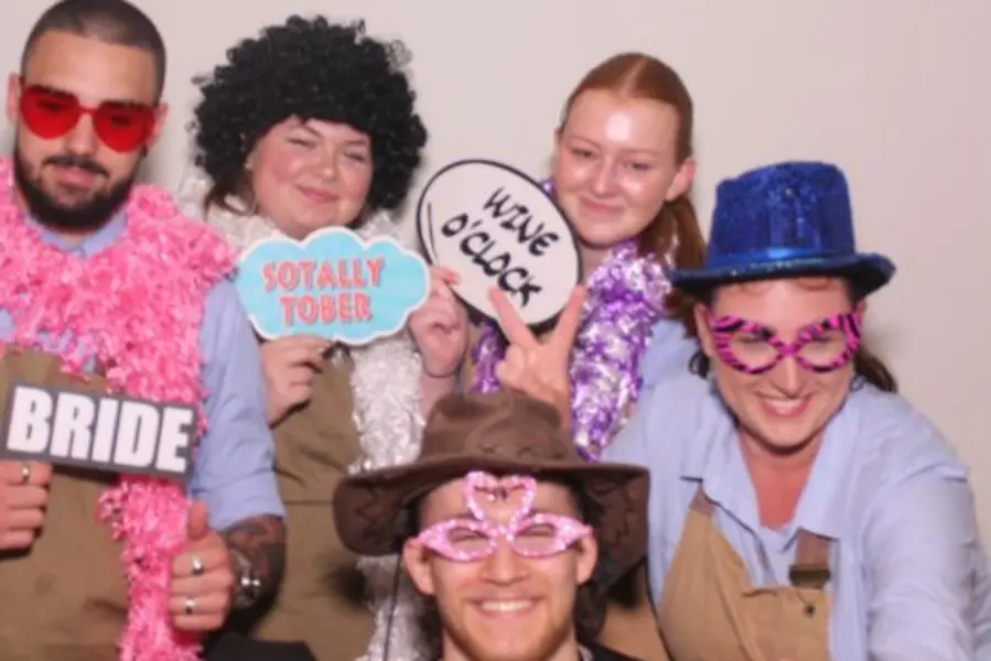 A group of guests crowding into the Limelite Photobooth with colourful glasses, hats and signs