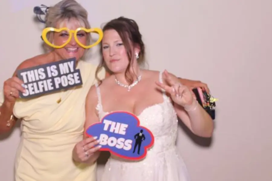 A bride and guest posing together in the Limelite Photobooth with playful signs